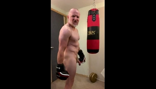Aggressive muscular boxer working out naked with a punch bag and cums on his boxing gloves
