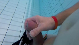 A fat guy wearing flamingo swim trunks masturbates underwater in a public pool with a rainbow band